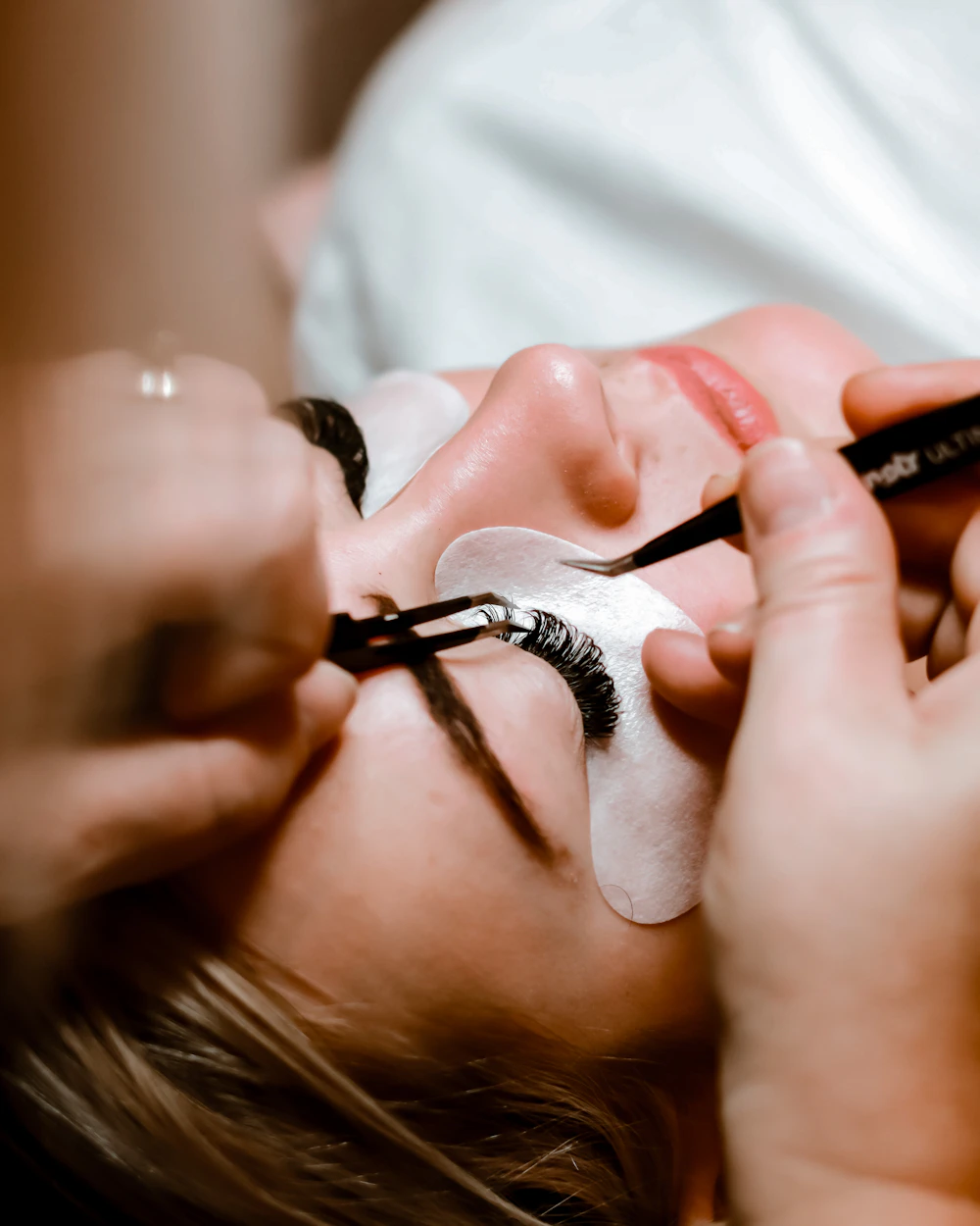 Lash technician applying individual eyelash extensions to a client with tweezers